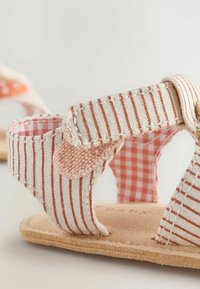 Raidatettu kankainen sandaalit beige- ja pehmeän vaaleanpunaisen värisinä, joissa on teksturoitu sulku ja ruudullinen vuori, sekä litteä, luonnollisen värinen pohja.