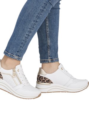 Person iført blå jeans og hvide platformsneakers med leopardprintdetaljer og sidelommer, gående på hvid baggrund.