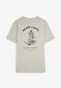 Beige Baumwoll-T-Shirt mit einem Grafikdruck auf der Rückseite. Das Design zeigt einen Cowboy-Stiefel, den Text "RODEO PARTY" und dekorative Sterne.