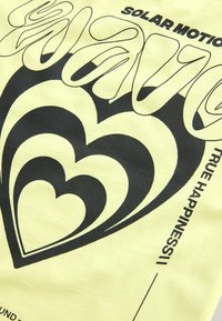Gul bomulds T-shirt med fed sort grafisk tekst og hjerte designs, med en glat tekstur og skærmtrykte detaljer.