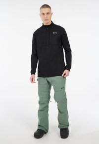 Čierny pulóver s polo zipom a textúrovanou hornou časťou, doplnený svetlozelenými snežnými nohavicami s vreckami na zips a nastaviteľnými manžetami.
