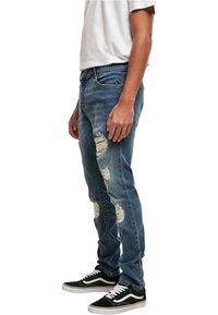 Modre kavbojske hlače z raztrganinami spredaj, slim fit, s srednjim pasom. Obute z črnimi in belimi supergami ter belim majico.