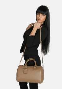 Borsa in pelle beige con finitura texturizzata, manici arrotondati e tracolla removibile. Presenta un'acca di etichetta e una forma strutturata.