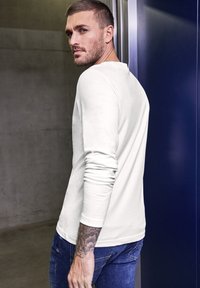 Långärmad, ljusgrå skjorta i bomull med rundad hals, figurnära design och uppvikt ärm, tillsammans med mörkblå jeans.