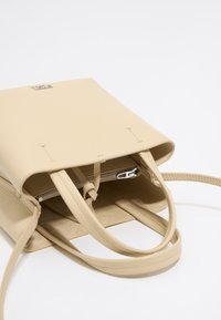 Beige leather handbag with dual handles, zippered closure, and textured surface. Interior features a soft lining and practical storage.