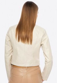 Giacca in pelle beige con design cropped, caratterizzata da cuciture decorative e maniche aderenti, abbinata a pantaloni beige.