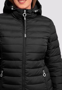Chaquetón negro tipo puff con diseño acolchado, capucha con cierre de cordón y acentos de hardware plateado en los cremalleras.