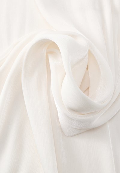 Tissu blanc transparent avec des plis doux et fluides disposés en un motif en spirale lâche sur une surface plane.