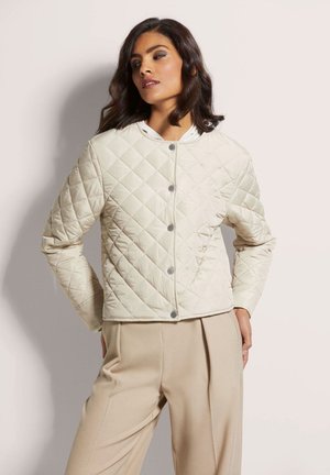 Gepolsterte Cremejacke mit rundem Ausschnitt, Knopfverschluss und langen Ärmeln; kombiniert mit beigen, weit geschnittenen Hosen. Glatte, gepolsterte Textur.