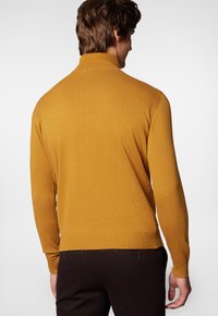 Sweter z golfem dzianym w musztardowym kolorze, z długimi rękawami i prążkowanym dołem, ukazany z tyłu na neutralnym tle.