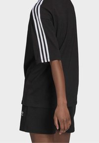 Black oversized t-shirt with white three-stripe design on shoulders. Paired with black shorts featuring a small white logo on the hem.