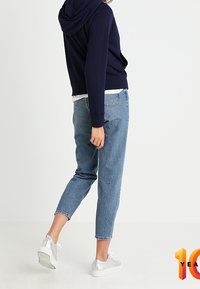 Marine capuchontrui, lichtblauwe cropped jeans en zilveren sneakers. Zachte stof, casual pasvorm en zichtbare stiksels op de jeans.