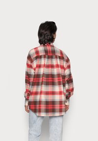 Chemise en flanelle à carreaux rouges, bruns et crème, manches longues, coupe décontractée, avec une couture djoke à l'arrière. Poignets boutonnés.