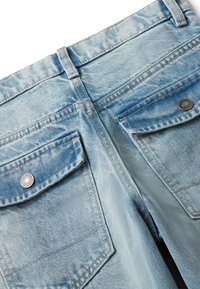 Světle modré džíny, pohled zezadu, se dvěma kapsami na klopě se zapínáním na kovové knoflíky a poutky na opasek.