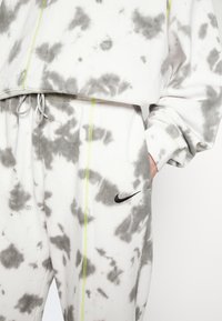 Vit och grå tie-dye sweatshirt och byxor med en svart Nike-logotyp, med en croppad design, dragsko och neonaccenter.