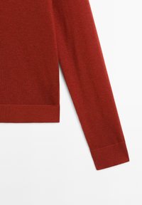 Sweter w kolorze rdzy z żebrowaną teksturą, z długimi rękawami i prostym wykończeniem, wykonany z miękkiego materiału. Bez dodatkowych wzorów ani akcentów.