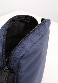 Borsa in tessuto blu navy con cerniera sulla parte superiore, caratterizzata da una superficie testurizzata e una fodera interna nera. Focalizzata su un design funzionale senza decorazioni.
