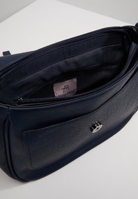 Granatowa torebka ze skóry z zamkiem błyskawicznym, wewnętrzną kieszenią oraz przednią kieszenią z okrągłym metalowym zatrzaskiem. Wewnątrz widoczna metka.