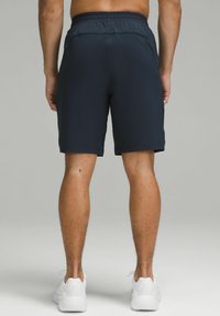 Navy blue athletic shorts made from lightweight material, featuring an elastic waistband and a mid-thigh cut, paired with white sneakers.