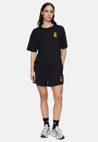 Zwart katoenen t-shirt en short set met een geel logo op de linkerborst en linker dij, met een relaxte pasvorm en korte mouwen.