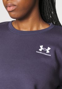 Sudadera azul marino fabricada en un material suave con un cuello redondo. Incluye el logo blanco de "Under Armour" en el área del pecho izquierdo.