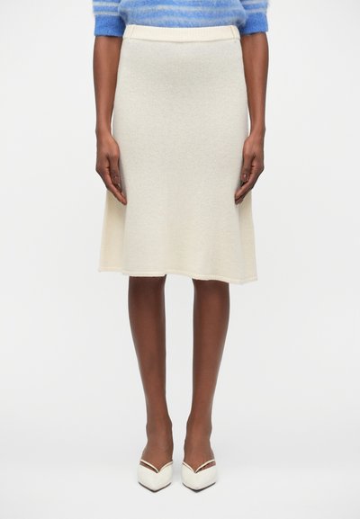 Gehaakte uitlopende rok in crème, met een zachte textuur, een nauwsluitende taille en subtiele naaddetails. Gepaard met witte spitse hakken.