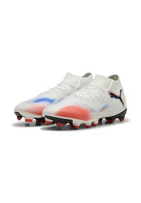 Botas de fútbol blancas con acentos degradados en rojo y azul, parte superior de tejido, collar tipo calcetín y tacos negros sobre una suela blanca. Logotipo de Puma visible.