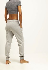 Camiseta atlética gris recortada combinada con pantalones de chándal gris claros que cuentan con puños elásticos y bolsillos laterales, con una textura de algodón suave.