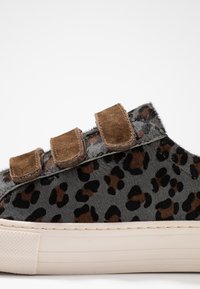 Tenisky s leopardím vzorem z šedé kožešiny, doplněné hnědými semišovými suchými zipy. Gumová podrážka s texturovanými detaily. Zaoblený design.