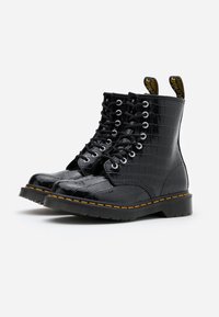 Svarta fusk krokodil läder ankelboots med rund tå, snörning fram, metallöglor och gul söm runt sulan.