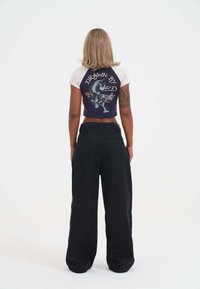 Camiseta recortada blanca y azul marino con gráfico y texto en la parte posterior, combinada con pantalones vaqueros de tiro alto y pierna ancha en negro. Tejido suave.