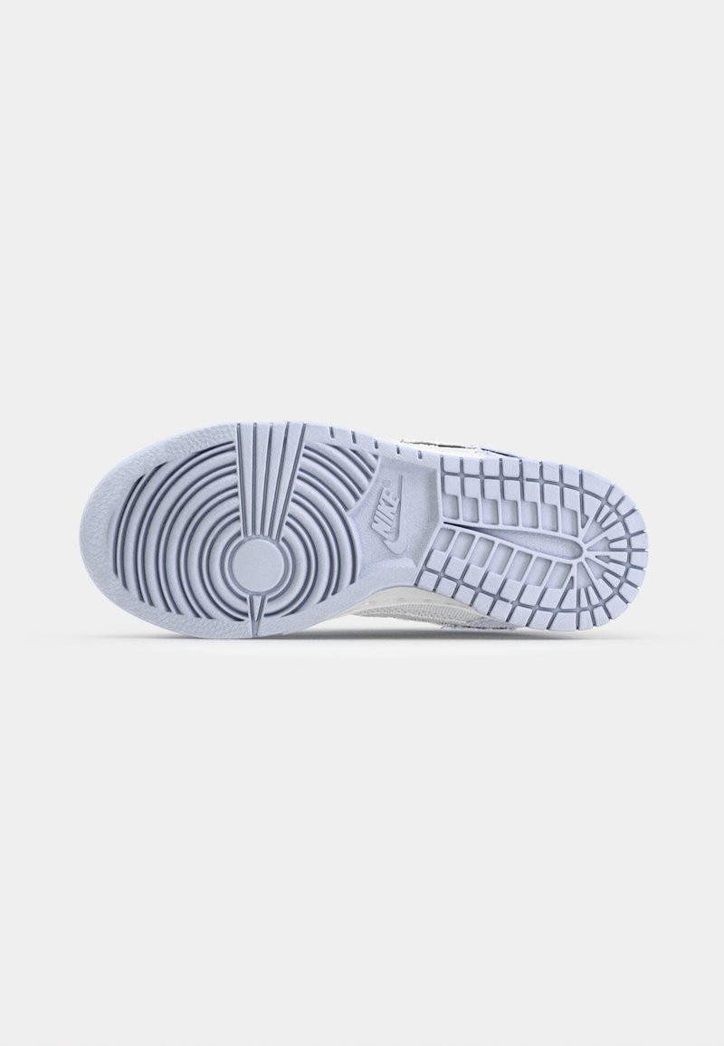 Suela de una zapatilla Nike blanca con patrones de tracción circulares y rectangulares y logotipo de Nike visible sobre un fondo blanco.