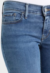 Vaqueros de mezclilla azul con una textura suave, cintura a media altura, diseño de cinco bolsillos y detalle de costura en contraste a lo largo de las costuras y los bolsillos.