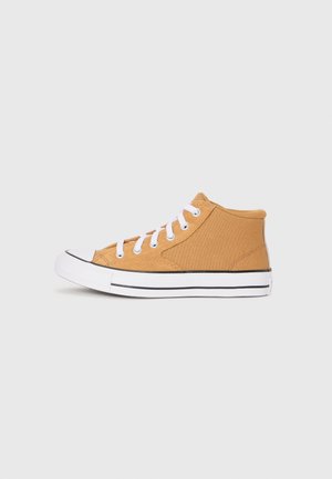 Zapatilla de lona de caña alta color marrón claro con suela de goma blanca y cordones blancos, vista de lado sobre un fondo gris claro.