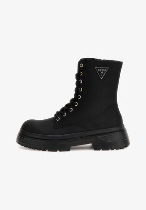 Bottine noire à lacets avec un bout rond, semelle en caoutchouc, tige texturée, œillets argentés et un patch logo triangulaire au niveau de la cheville.