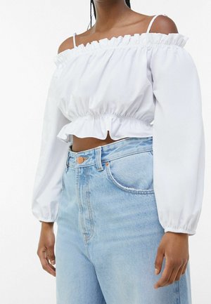 Woman wearing white off-shoulder long-sleeve crop top with elastic waist paired with high-waisted light blue jeans.