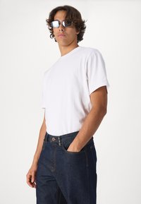 T-shirt en coton blanc à col rond, associé à un jean en denim foncé avec des coutures orange et une fermeture à bouton visible.