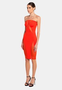 Rotes schulterfreies Bodycon-Kleid mit Netz-Ausschnitten, figurbetontem Schnitt, knielangem Saum und glatter Textur. Getragen mit schwarzen High-Heels.