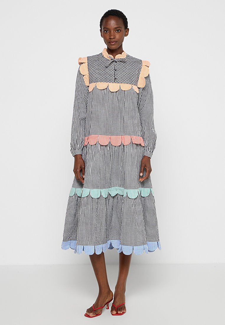 Vestido de cuadros en blanco y negro con acentos de pasteles en rosa, azul y verde. Mangas largas, tapeta de botones y diseño de falda en capas.