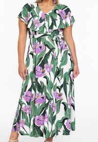 Maxikjol med V-ringning, korta flygande ärmar, gröna blad och lila blommor på vit bakgrund; inkluderar midjesnodd för passform.