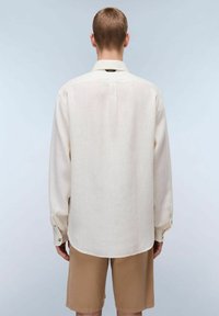 Camicia a maniche lunghe di colore crema, realizzata in tessuto leggero, con colletto classico e polsini con bottoni, caratterizzata da un orlo curvo.