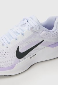 Nike løpesko med en hvit mesh-overdel med lavendel detaljer, svart swoosh-logo og teksturert såle for grep. Ventilasjonsperforeringer inkludert.