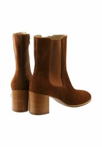 Bottines en daim marron avec des panneaux élastiques sur les côtés et un bout arrondi. Elles présentent un talon en bloc de bois et une doublure intérieure lisse.