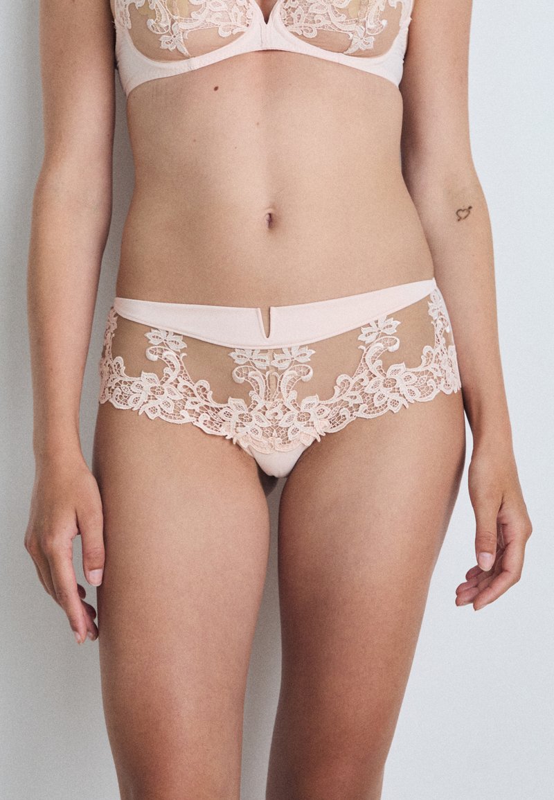 Krajkové prádlo v jemnej ružovej farbe. Podprsenka má priesvitné kvety a nohavičky majú podobný dizajn s hladkým pásom.