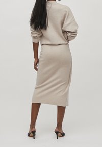 Béžový pletený svetr a midi sukně, s volným střihem, žebrovanými manžetami a bočním rozparkem, doplněné černými lodičkami s otevřenou špičkou.