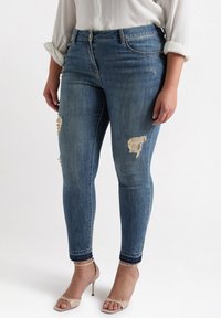 Blue denim skinny jeans with distressed detailing and frayed hems, paired with nude heeled sandals.