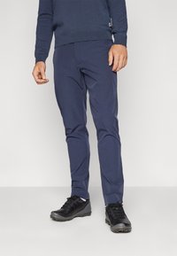Pantalons bleu marine au design ajusté, fabriqués dans un tissu lisse. Associés à des chaussures noires avec une semelle texturée et des lacets.
