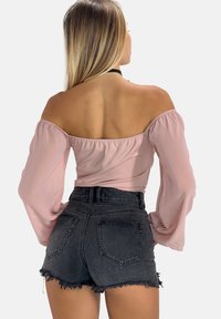 Off-the-shoulder lyserød bluse med lange, puffede ærmer, parret med højtaljede sorte denimshorts med frynset kant.