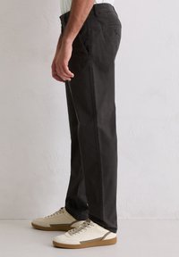 Czarne spodnie o prostych nogawkach wykonane z bawełny, z bocznymi kieszeniami i tylną kieszenią na guzik, zestawione z kremowymi sneakersami o fakturowej podeszwie.