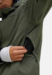 Groene waterdichte jas met een voorzak met rits, verstelbare manchetten en een slank ontwerp, dat gladde stof en minimalistische accenten toont.